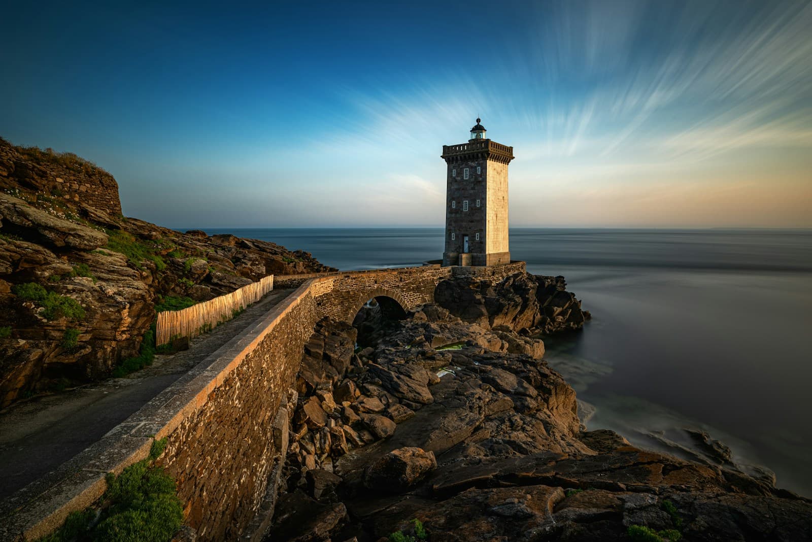 A lighthouse standing on a rocky coastline at dusk